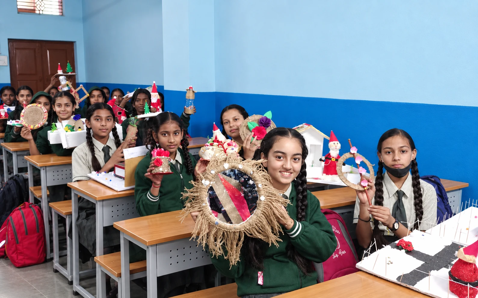 Girl students displaying handmade creative craftwork and mirror art in classroom at Alpha English H.S. School