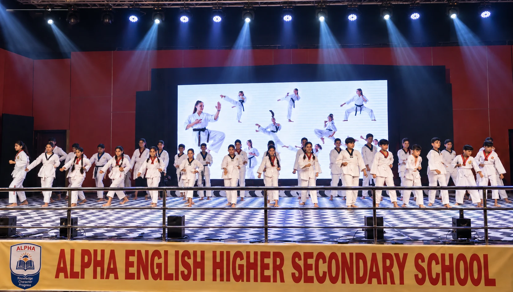 Students performing synchronized karate martial arts and self-defense routine on stage in front of Alpha English H.S. School banner